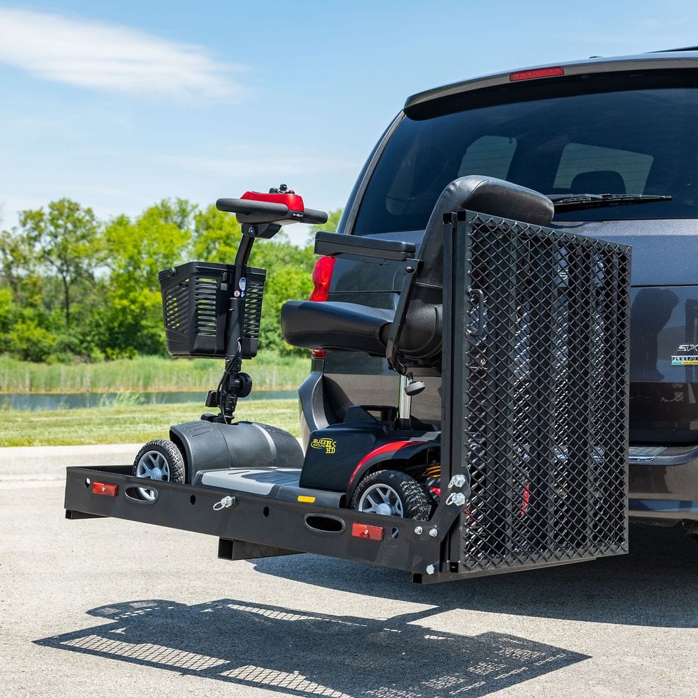 The back of an SUV. There is a platform attached to the back of it, on the platform is a mobility scooter.
